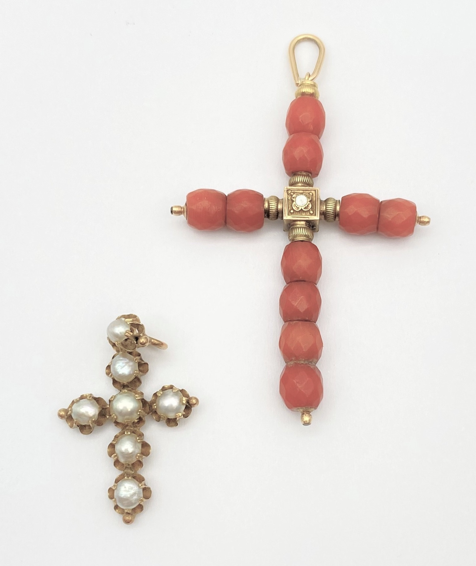Deux croix-pendentif en or 18K, l'une agrémenté de demi-perles, l'autre de billes de corail facettées 