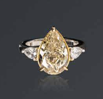 Bague en or 18K (750), ornée d'un diamant jaune pâle taillé en goutte pesant 6,02 cts épaulé de deux diamants blancs